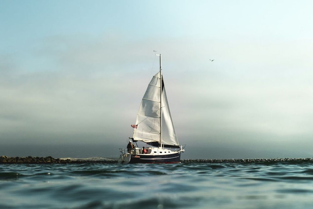 A white and black sailboat resting on calm water under a soft sky.