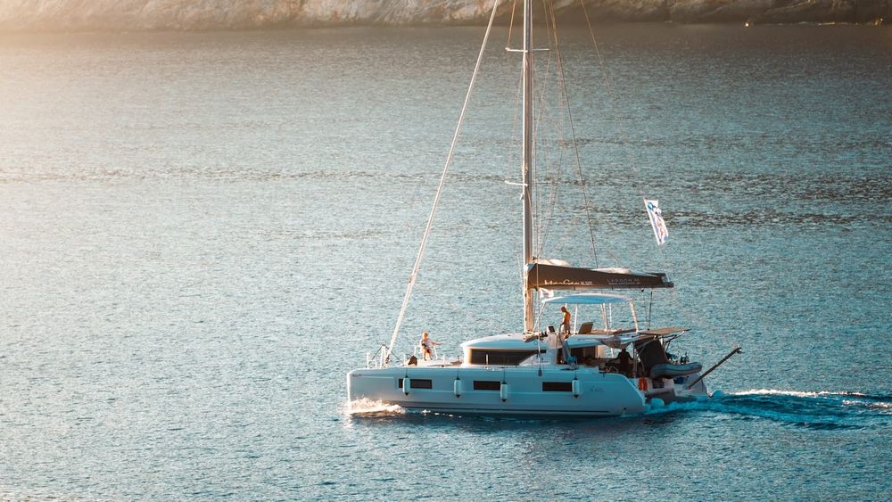 A cruising catamaran motoring slowly through a calm anchorage in golden evening light, sails furled
