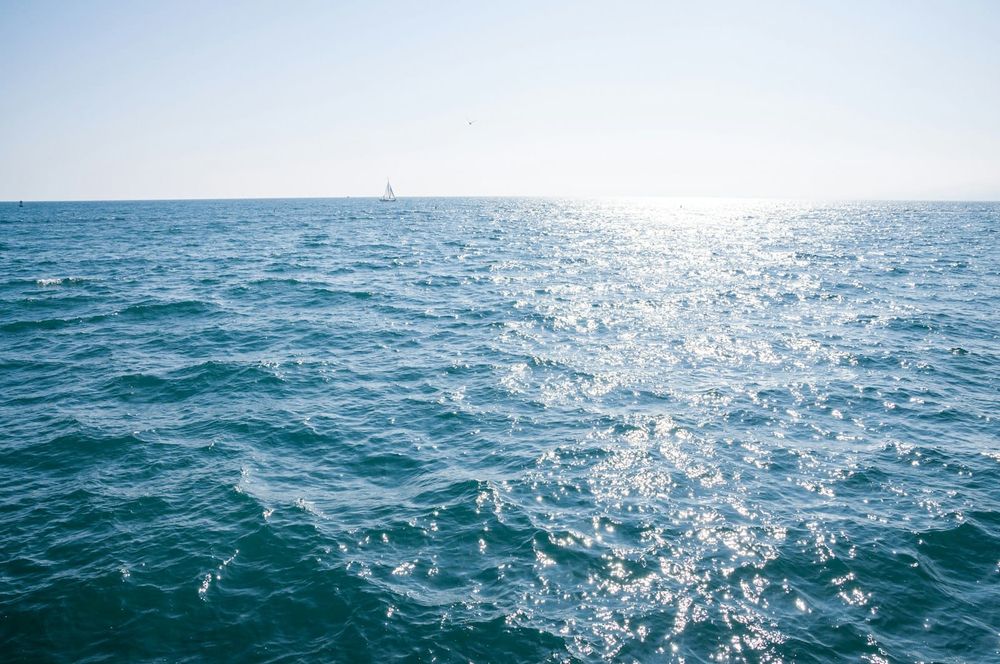 A lone sailboat on the horizon of an empty, sunlit open ocean