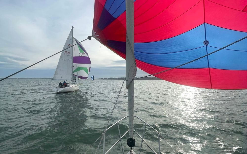 Red and blue spinnaker flying from the bow, with another yacht running downwind under spinnaker nearby