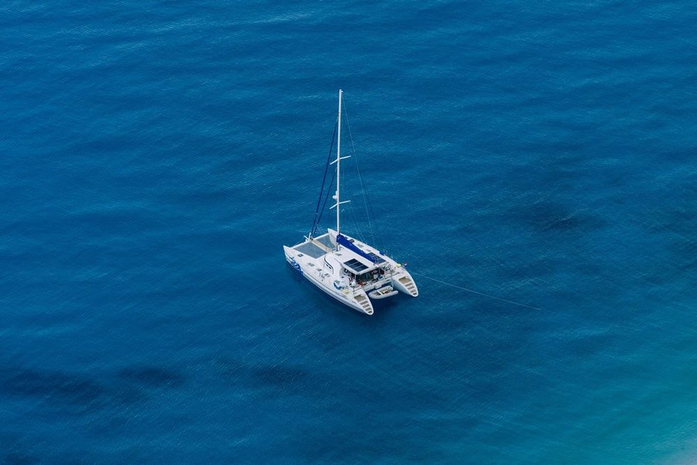 A cruising catamaran alone on open blue water, seen from above
