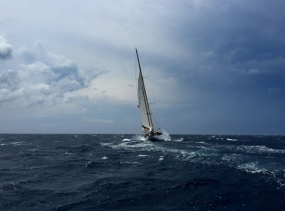 A sloop sailing upwind through whitecapped dark-blue seas under a heavy, darkening sky