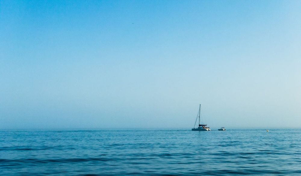 A white sailboat on open blue ocean under a clear sky, the kind of settled conditions you wait for before leaving Tonga for New Zealand