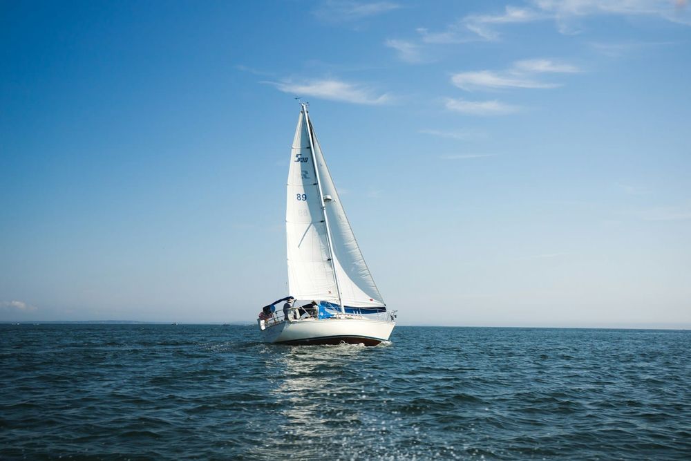 A white sailboat under full sail on open blue water with a clear sky