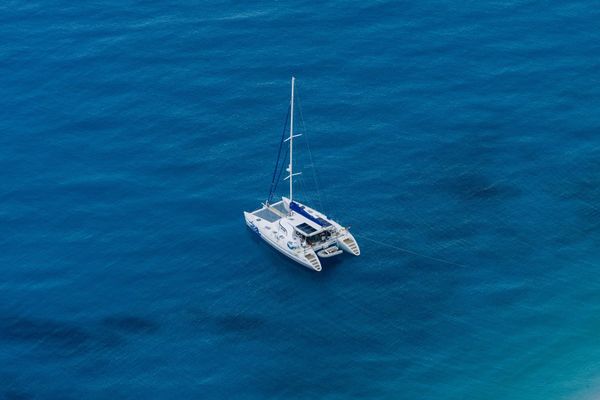Cruising catamaran anchored alone in turquoise water, viewed from above