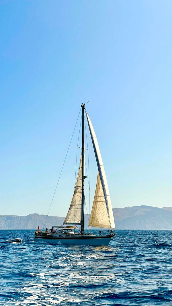 Cruising sloop close-reaching offshore with mountains on the horizon