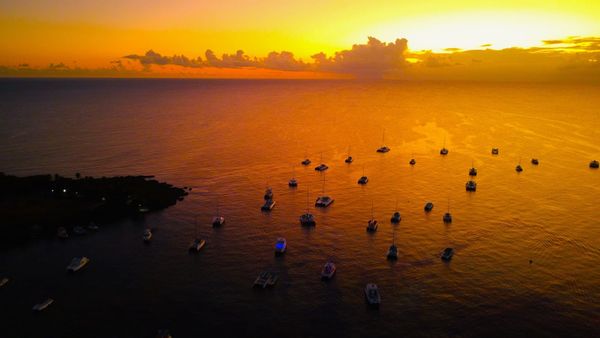 Catamarans and sailboats anchored in a tropical bay at sunset, viewed from above