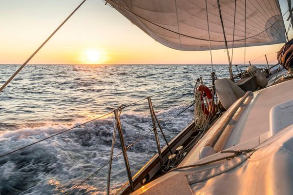 A monohull sailing yacht heeled over on a beam reach at sunset, viewed from the deck looking aft toward the horizon