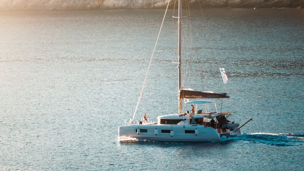 A cruising catamaran motoring slowly through a calm anchorage in golden evening light, sails furled