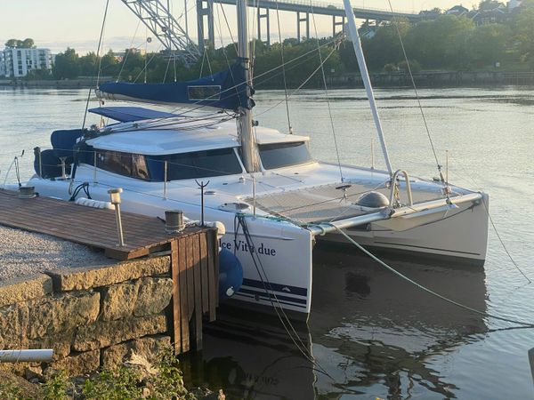 A white cruising catamaran lying alongside a dock in calm water under a clear sky