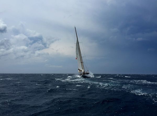 A sloop sailing upwind through whitecapped dark-blue seas under a heavy, darkening sky