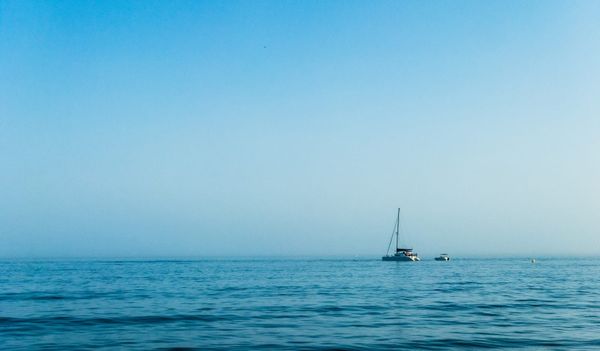 A white sailboat on open blue ocean under a clear sky, the kind of settled conditions you wait for before leaving Tonga for New Zealand