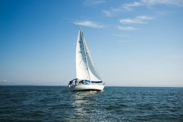 A white sailboat under full sail on open blue water with a clear sky