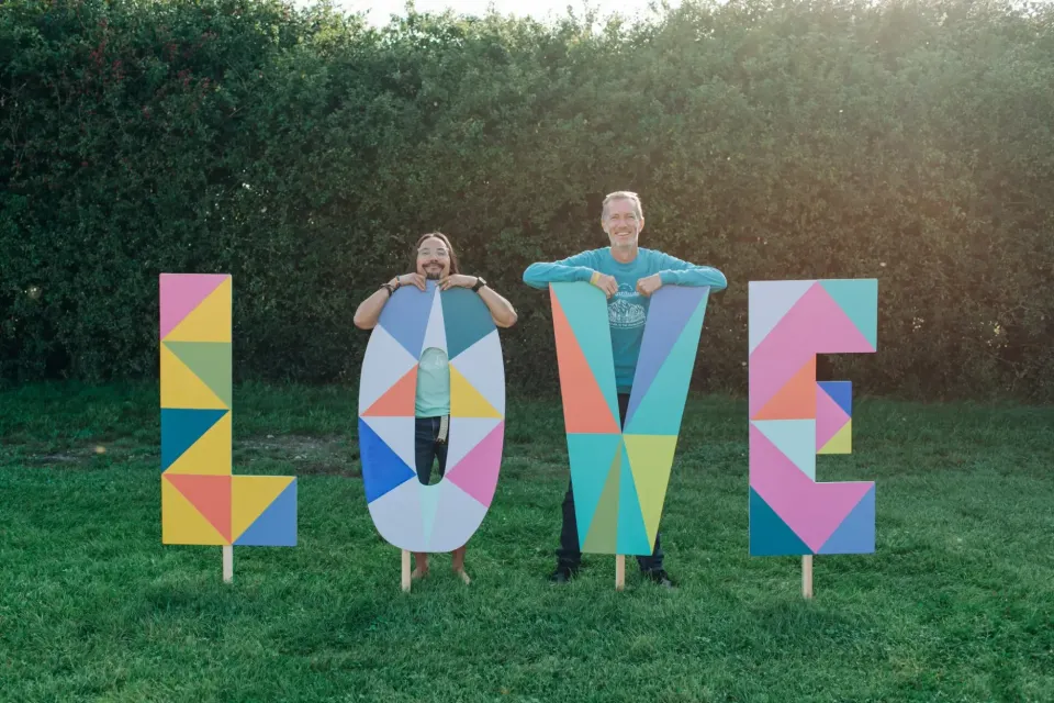 Two people pose outdoors behind large colourful LOVE letters at a Happy Startup School event.