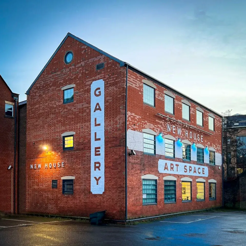 Red-brick New House Art Space building at dusk with painted Gallery, New House and Art Space signs beside the car park.
