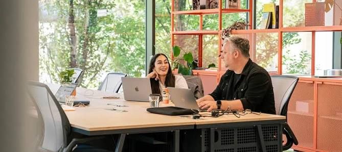 Two people working on laptops at a shared table in the Plus X Innovation Brighton coworking space.