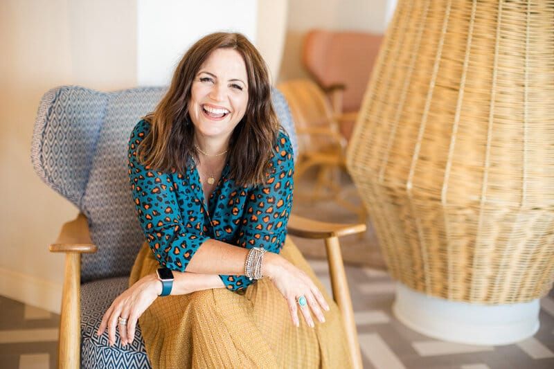 Vicki Knights sitting in a patterned armchair and smiling at the camera in a bright interior.