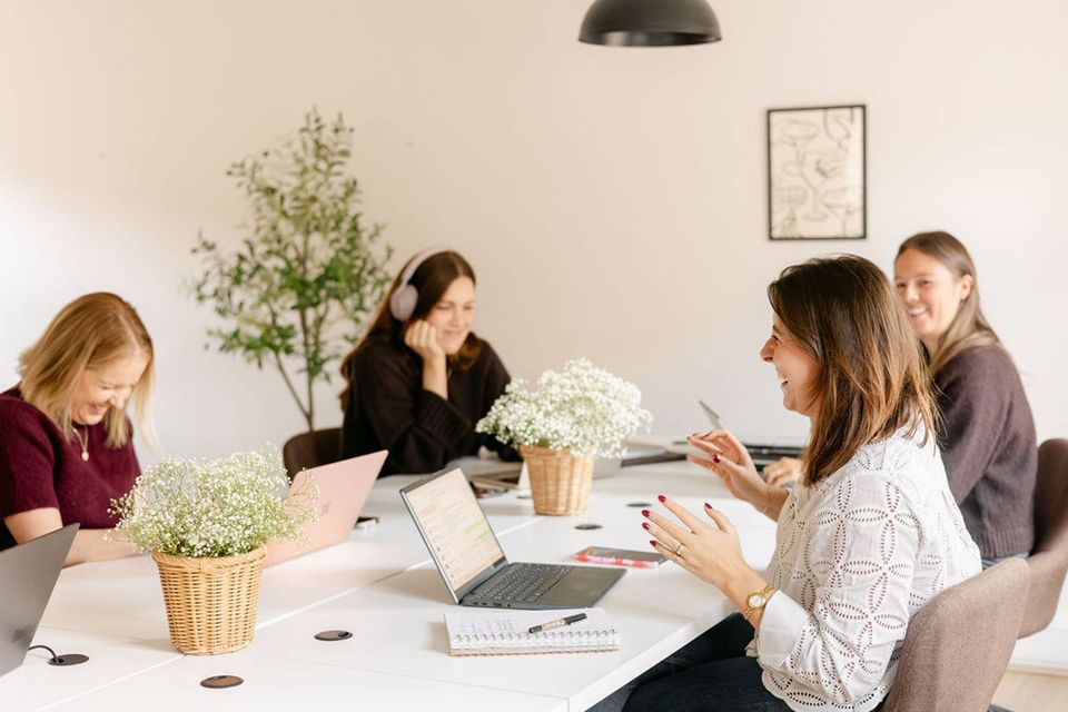 Four women working and talking around a shared table inside Village Coworking in Farnham.