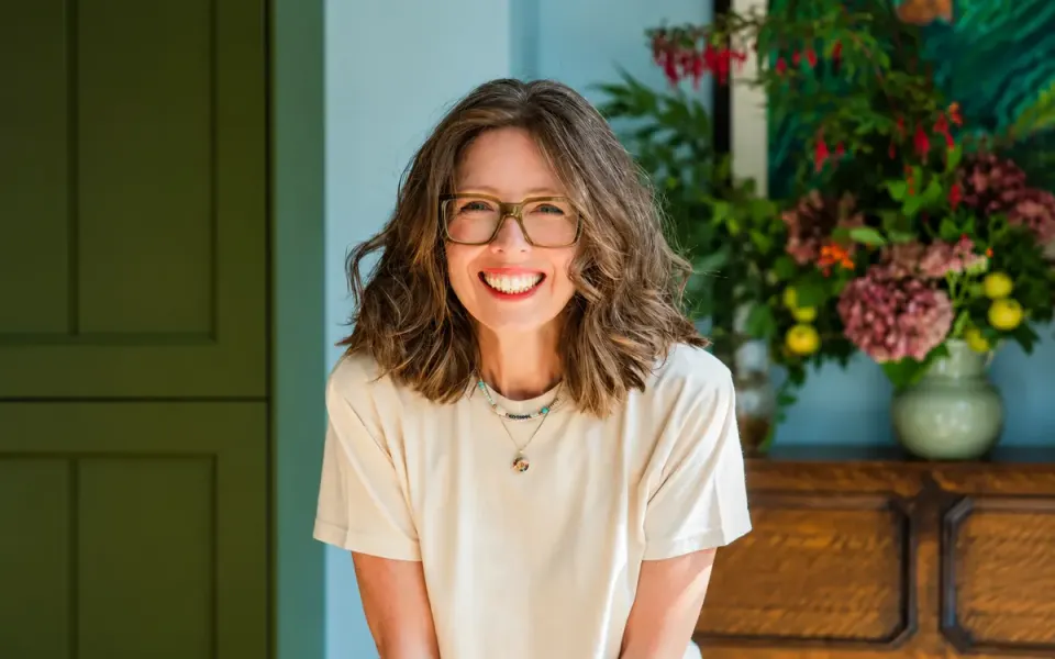 Clare Yarwood-White smiling in a room with flowers and a pale blue wall.