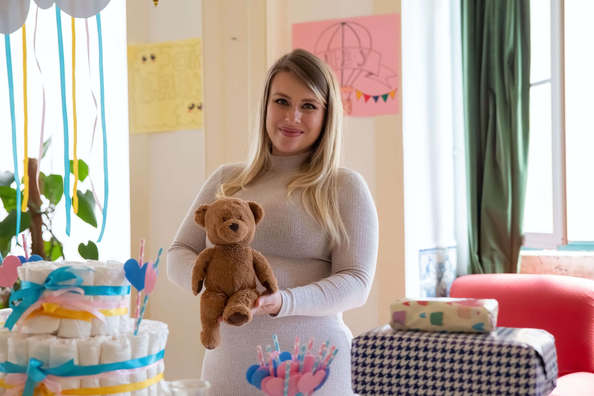 Blivande mamma bredvid en blöjtårta med en nalle i famnen