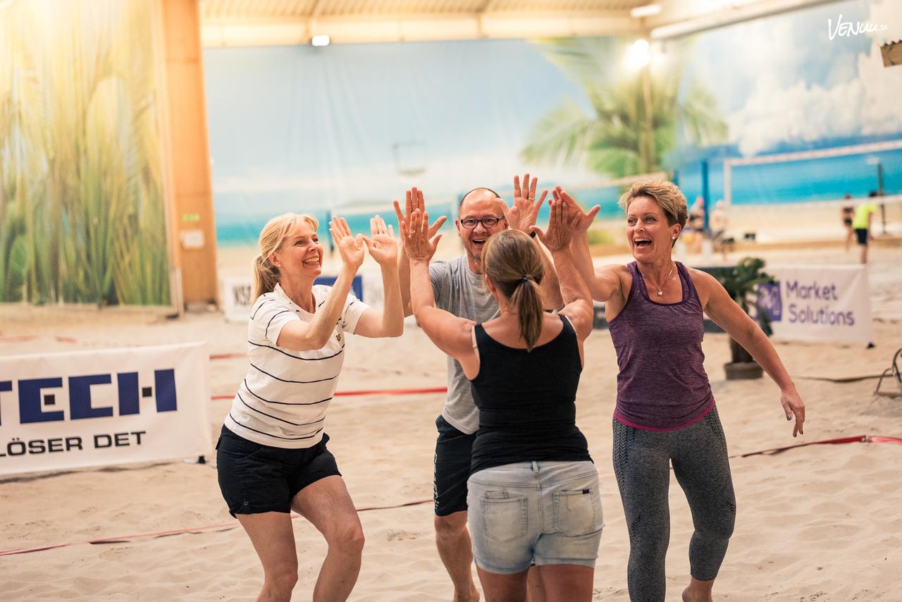 En actionfylld bild av kollegor som spelar beachvolleyboll på en inomhusplan med sand.