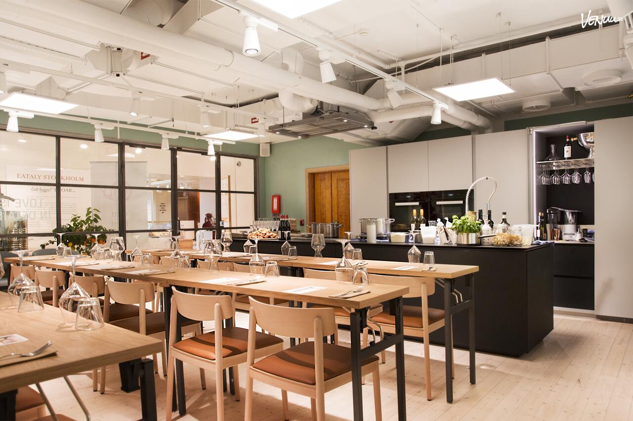 En italiensk matstudio med tegelväggar, en stor köksö och deltagare som lagar pasta och andra italienska rätter.