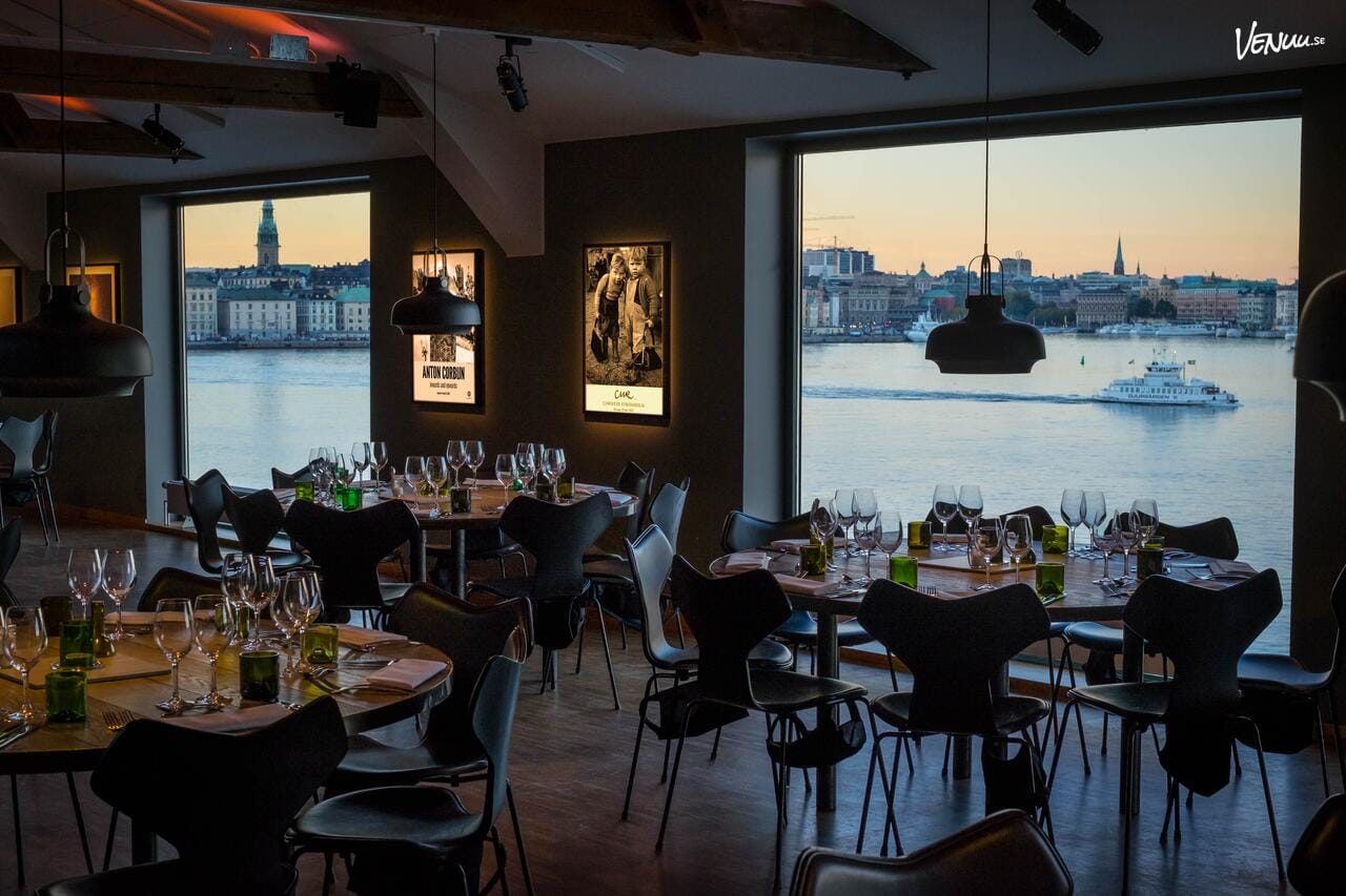 En elegant restaurang med modern inredning och stora fönster som erbjuder panoramautsikt över vattnet och staden.
