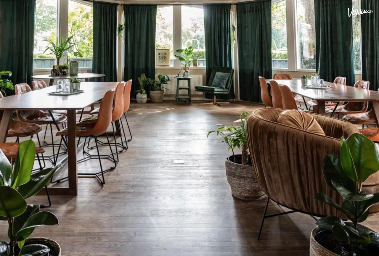 En ljus och grönskande paviljong med stora glaspartier och växter, som skapar en avkopplande miljö.