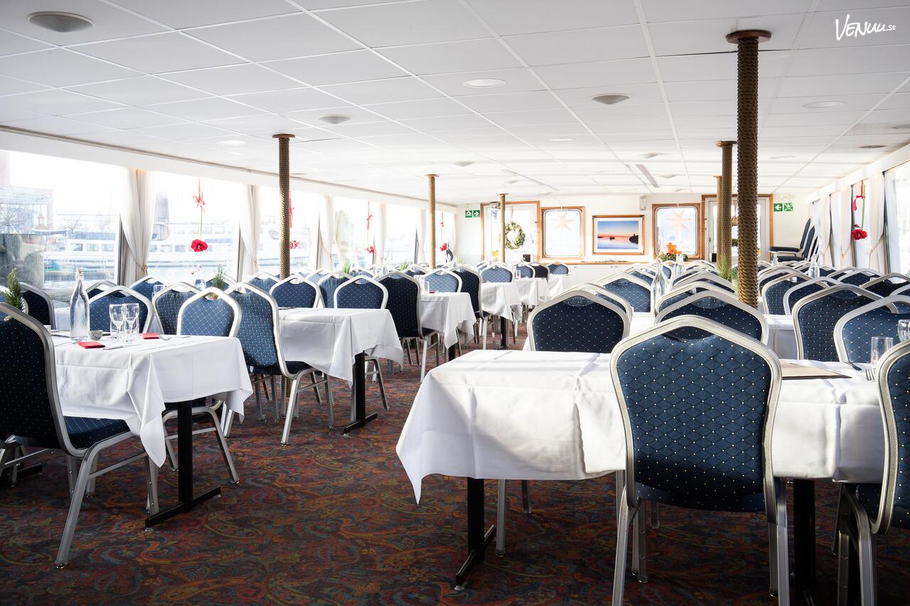 En modern festbåt med stora panoramafönster och ett övre soldäck, som glider fram på vattnet.