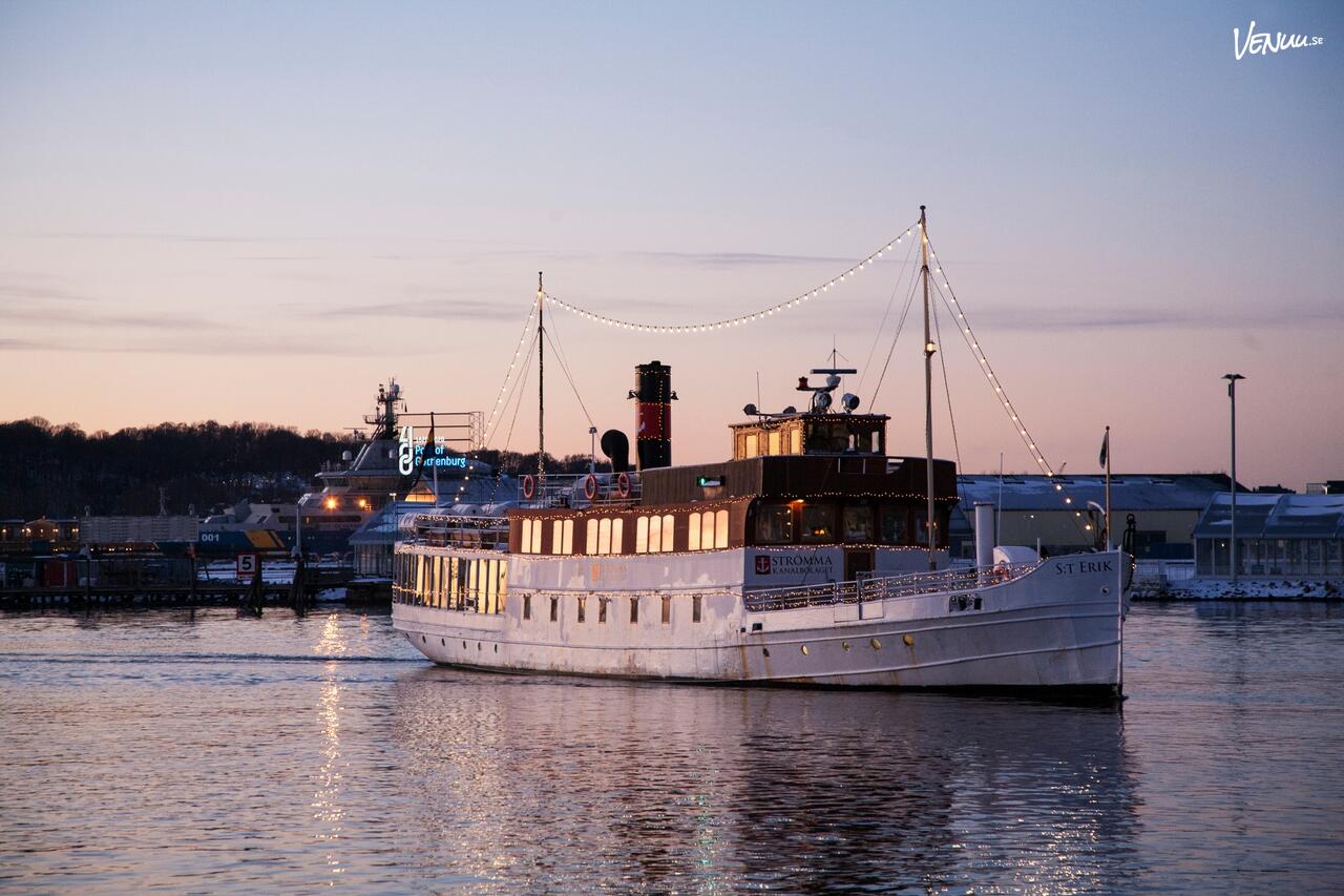 En klassisk, vit ångbåtsliknande festbåt med flera däck och passagerare på vattnet.