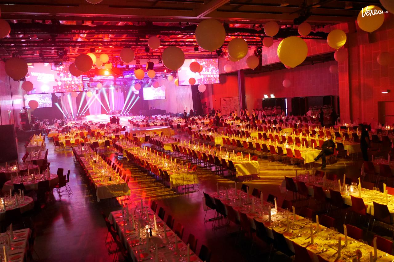 En livfull bild av en festlokal med modern inredning, scen och dansgolv med glada människor.