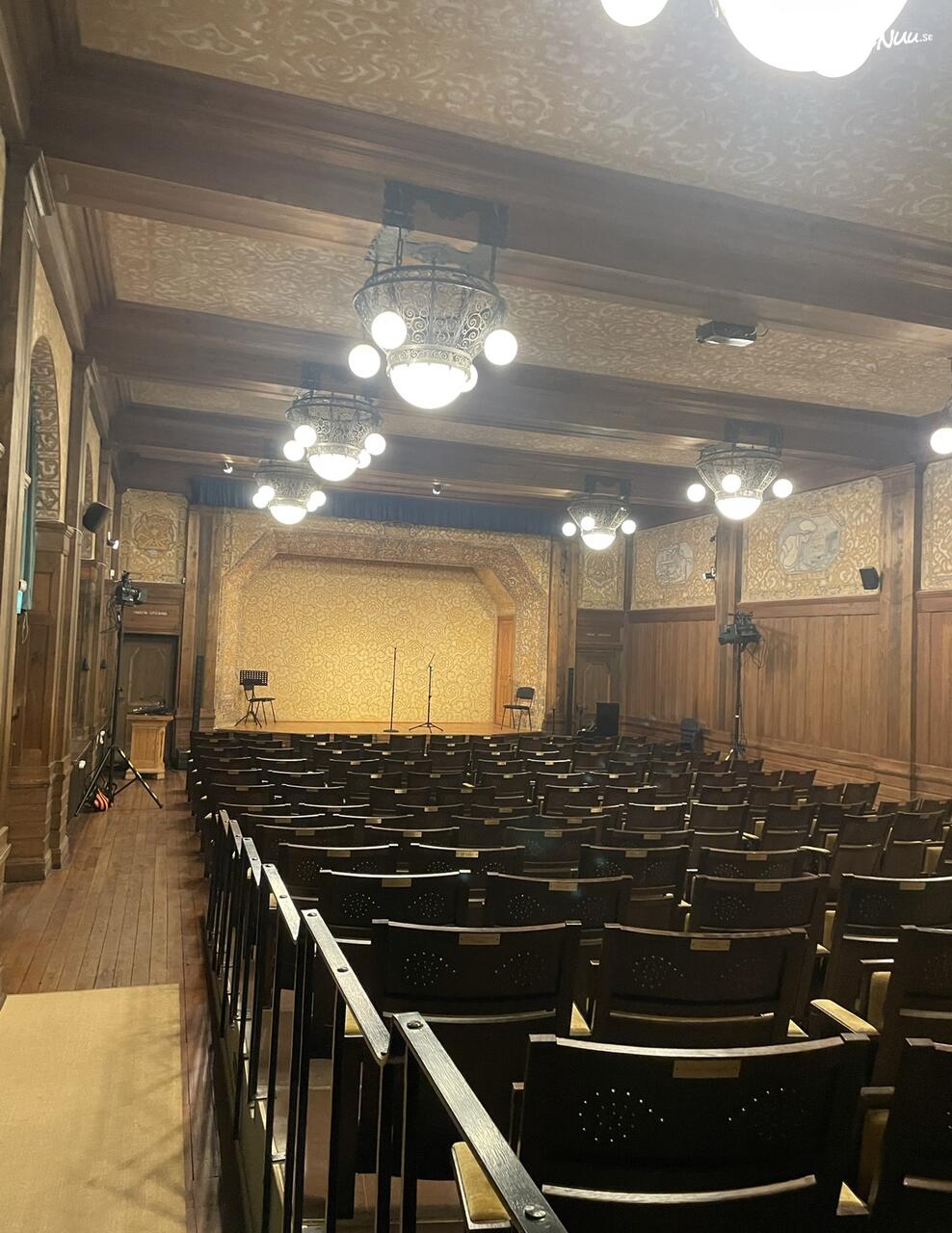En anrik biografsalong med klassiska biostolar, röd sammet och en stor filmduk.