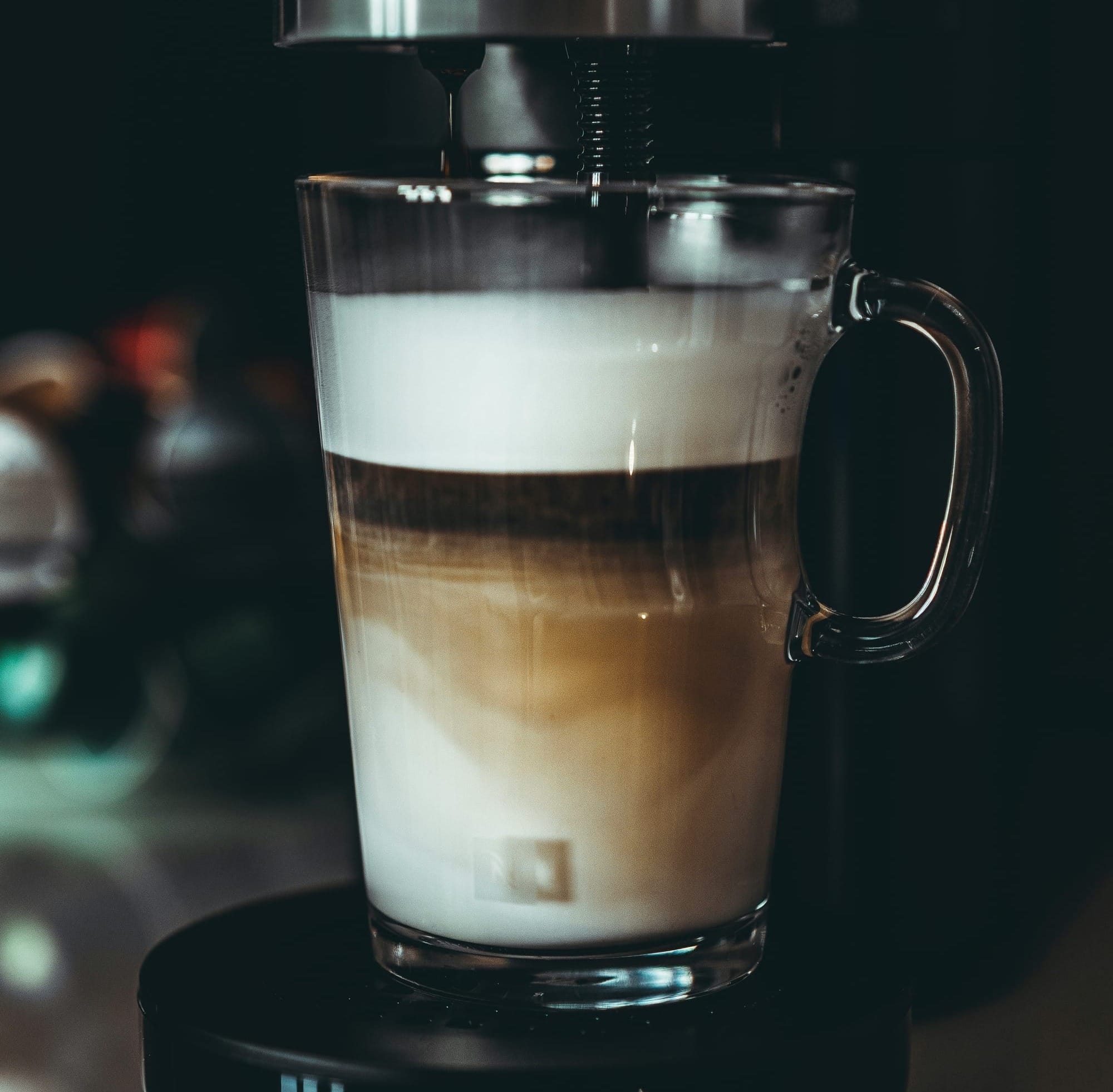 Ett glas med skiktad latte under bryggning i en kaffemaskin.