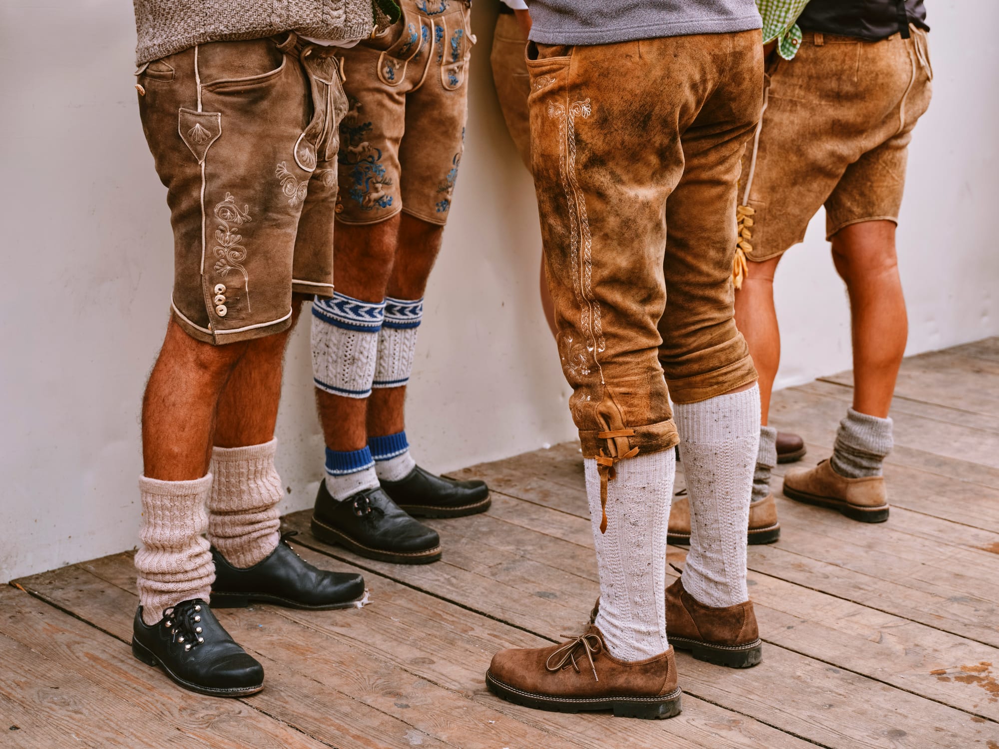 Detaljbild på flera män som bär traditionella lederhosen och speciella strumpor, vilket visar de detaljerade sömmarna och designen av en typisk oktoberfest outfit. Skorna och strumporna är också en viktig del av oktoberfest kläderna.