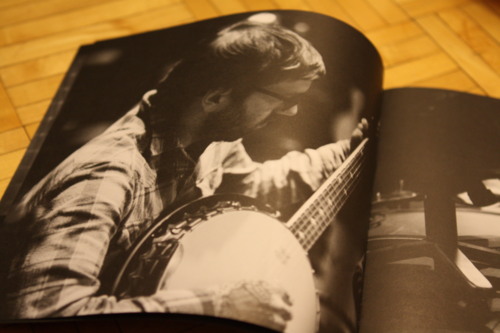 Dallas Green wearing a plaid shirt and glasses while playing a banjo in an album insert booklet.