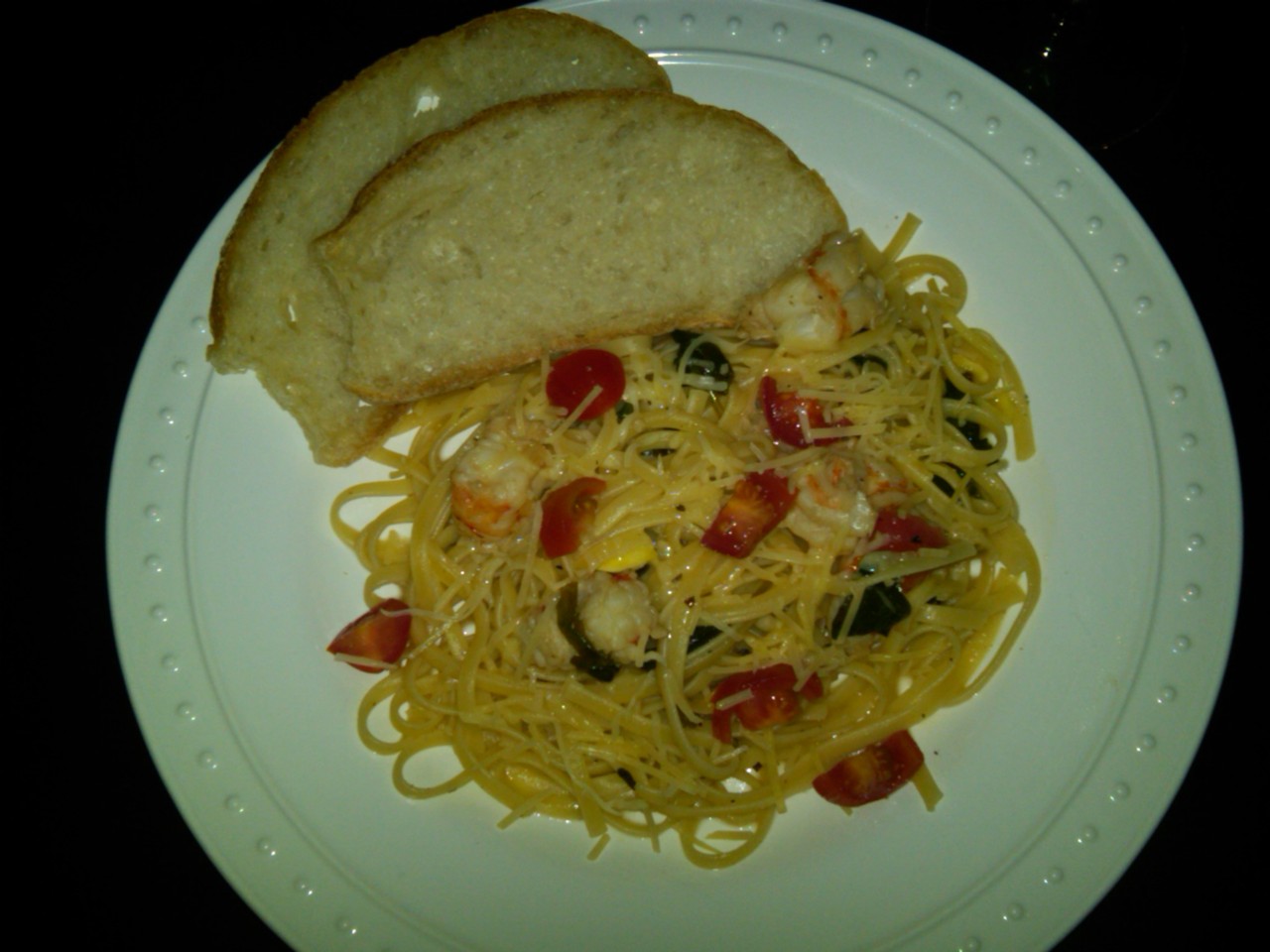 Shrimp linguine pasta garnished with tomatoes, herbs, and parmesan, served with rustic bread.