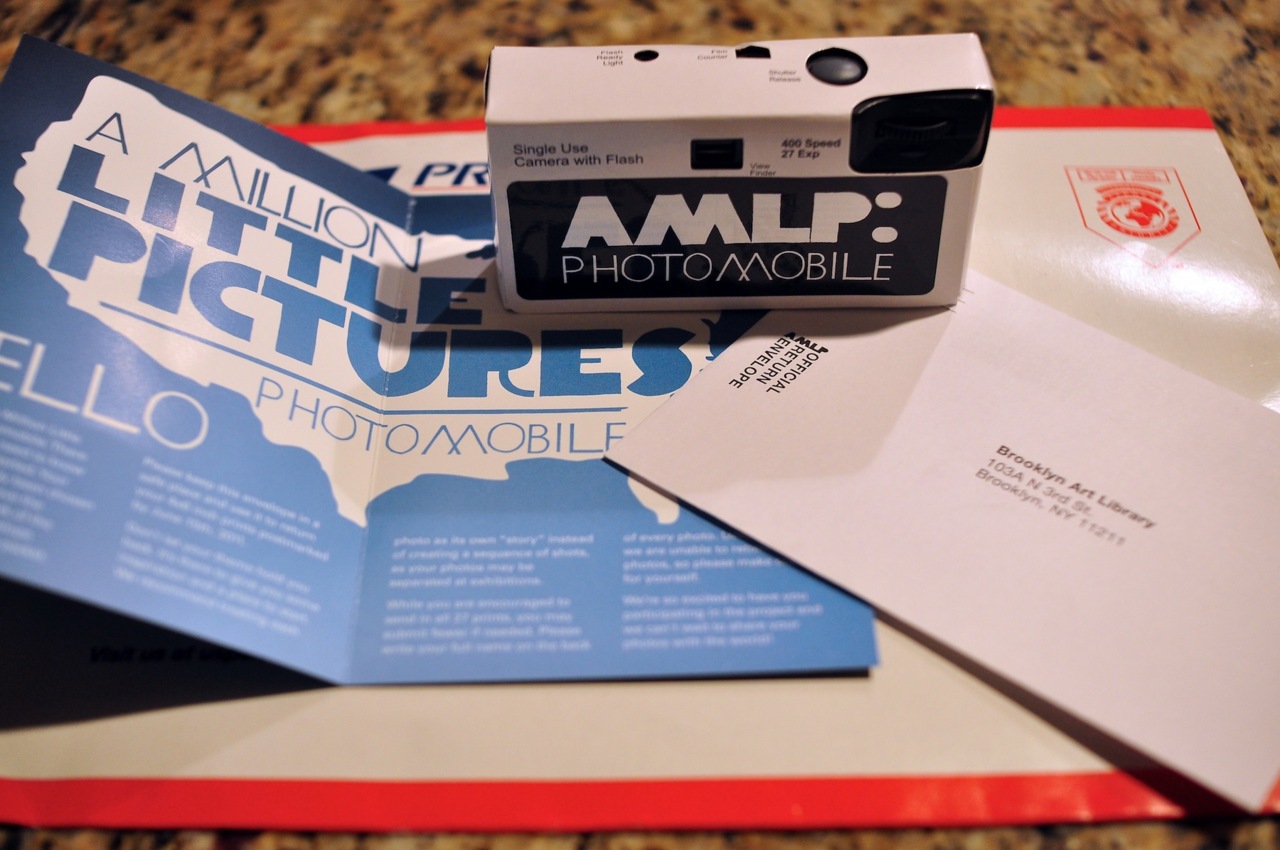 Disposable camera labeled AMLP: Photomobile beside a return envelope and informational pamphlet.