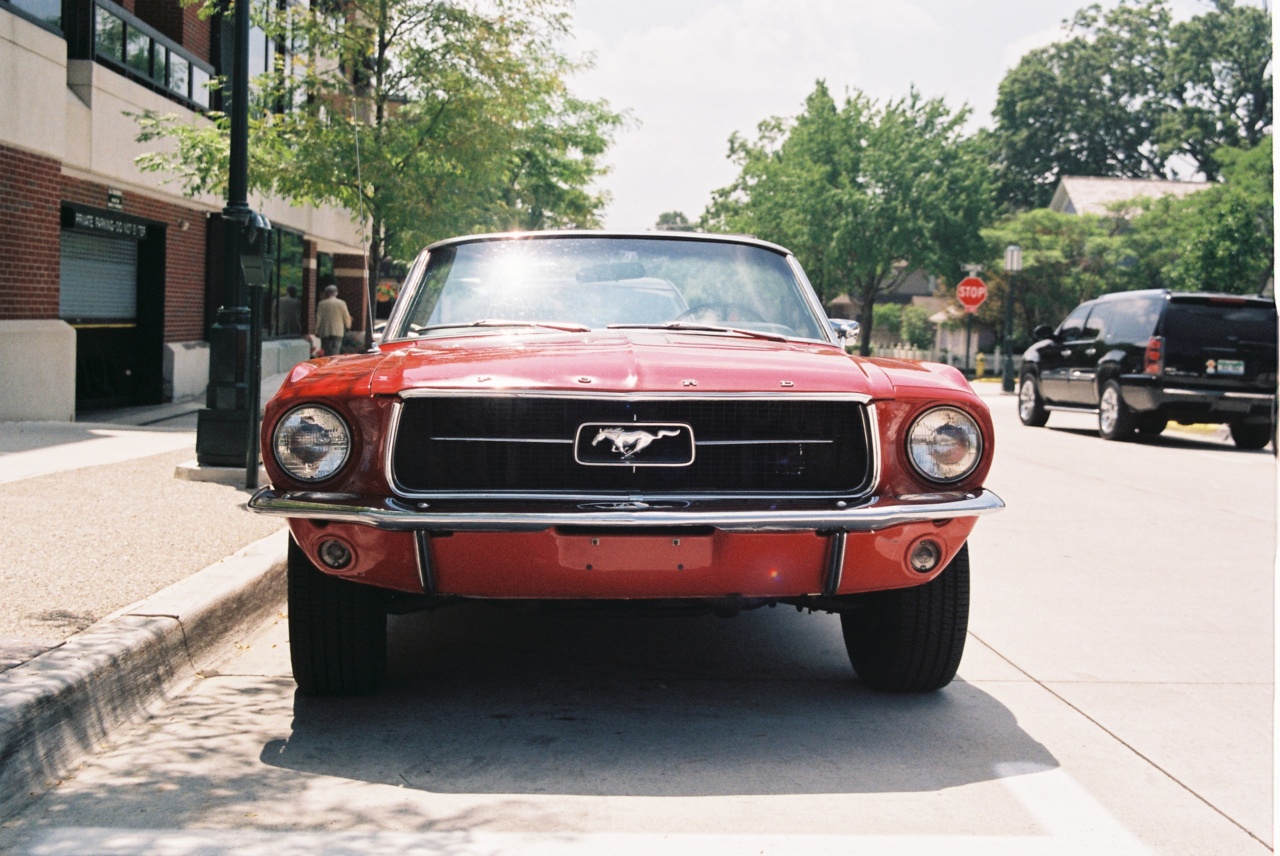 Red Ford Mustang convertible parked curbside in Michigan, showing chrome bumper and running horse emblem.