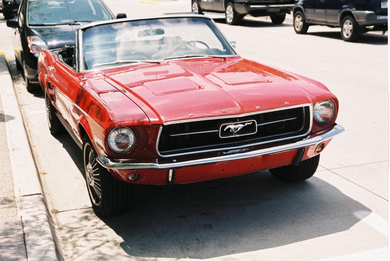 Front three-quarter view of a cherry-red vintage Ford Mustang convertible parked on a suburban street.