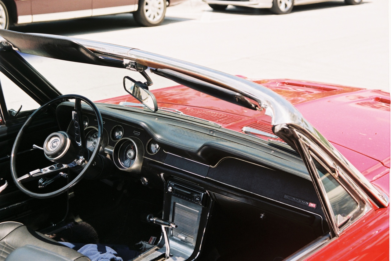 Open cockpit of a vintage red Ford Mustang convertible showing steering wheel, gauges, and console.