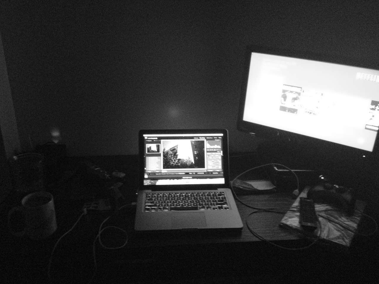 Desk setup at night with a laptop running Lightroom, external display showing Netflix, and a coffee mug.