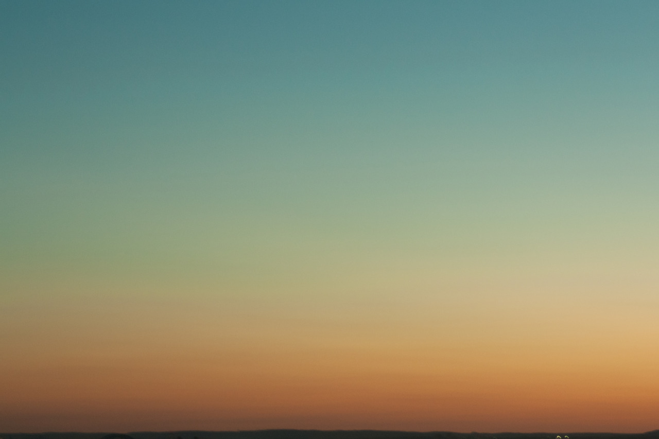 Gradient sunset sky transitioning from turquoise blue through pastel green to warm amber and orange.
