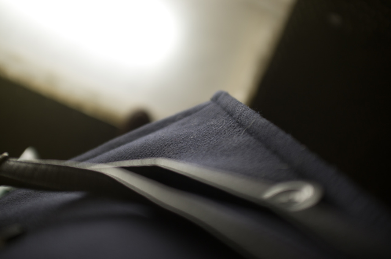 Macro close-up focusing on the seam of a dark wool jacket collar with soft out-of-focus background light.