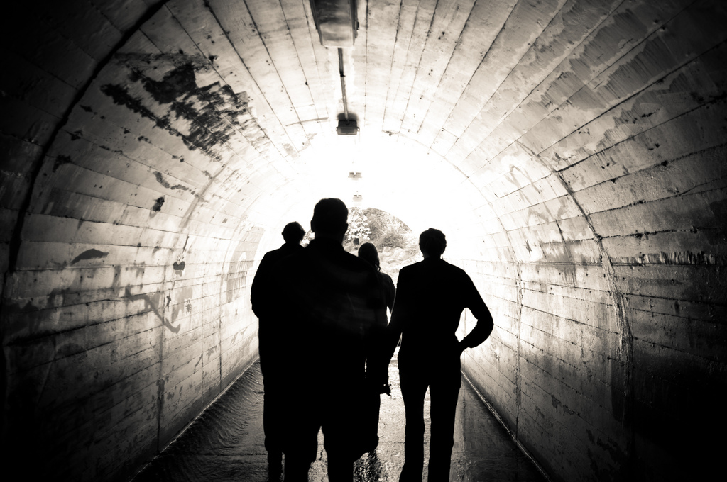 Four people walking through an arched concrete tunnel toward bright daylight at the opening.