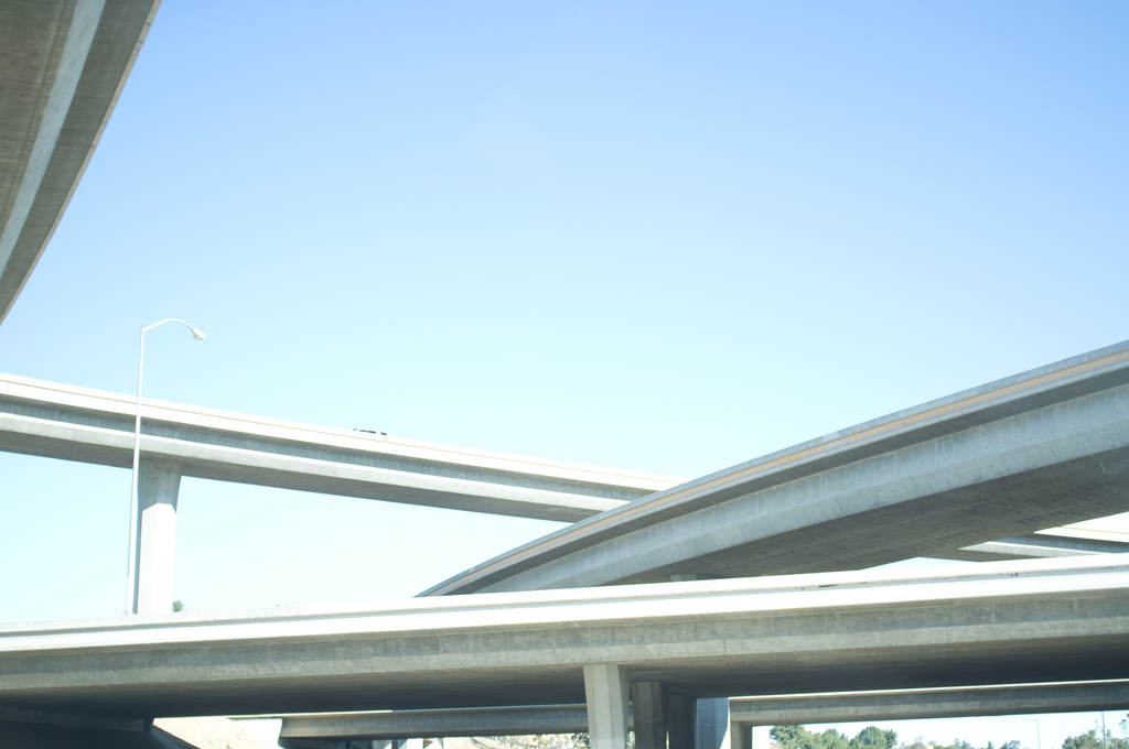 Intersecting freeway overpasses curving across a clear blue California sky with a car on the ramp.