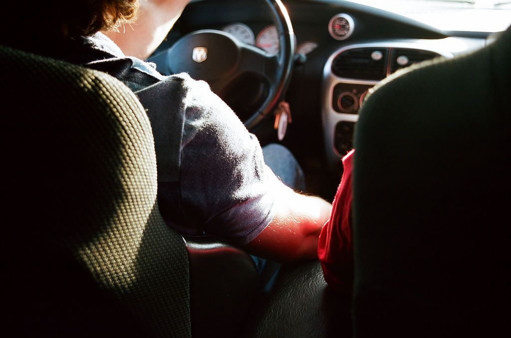 View from the back seat of a driver's sunlit arm gripping the steering wheel of a Dodge vehicle.