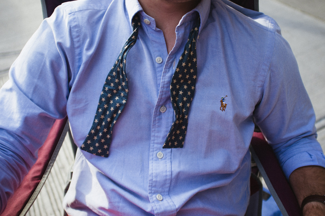 Untied navy blue bow tie with white stars draped across the open collar of an Oxford shirt.