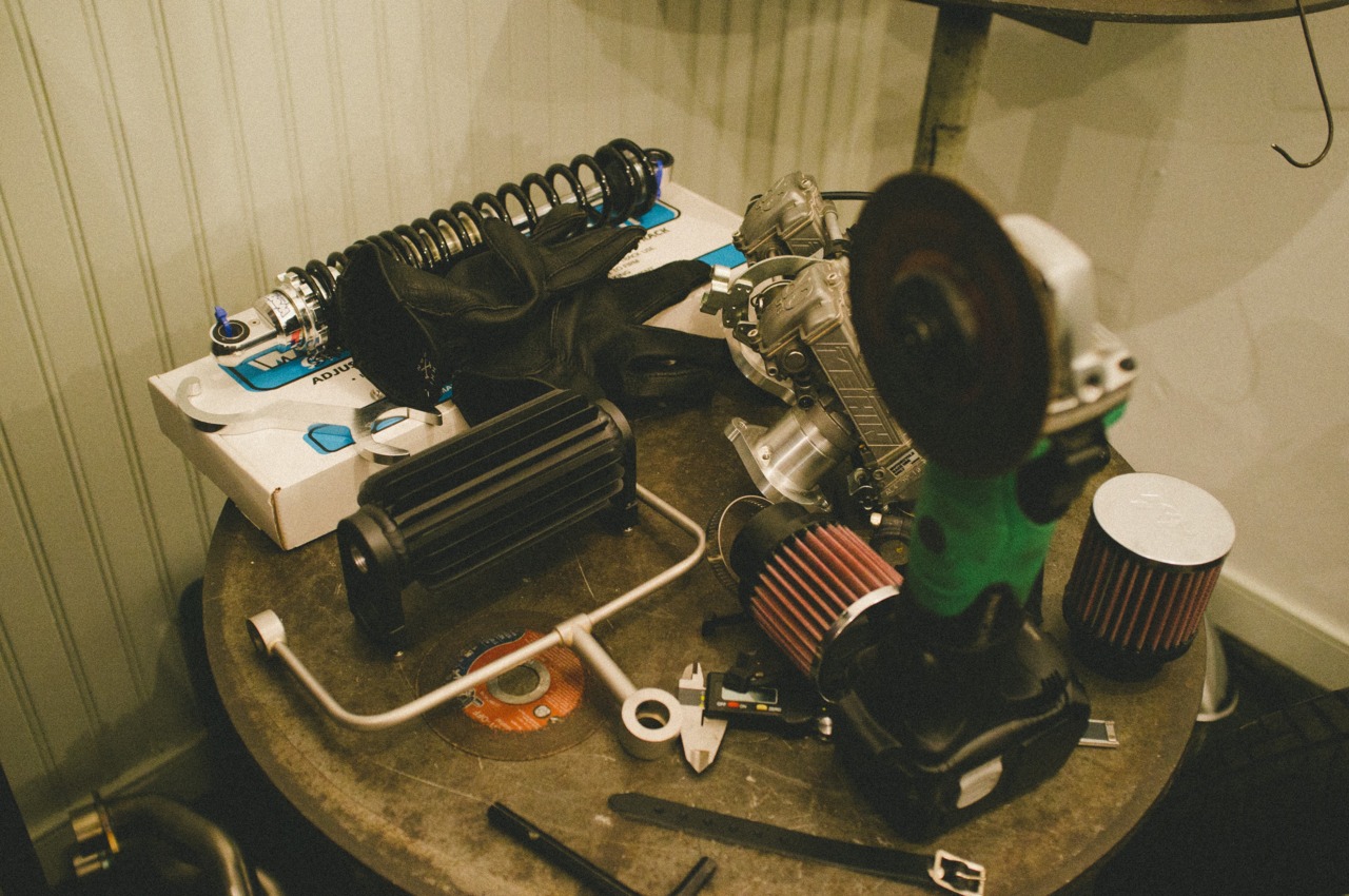 Custom motorcycle parts, suspension shock, cone air filters, and tools arranged on a round wooden table.