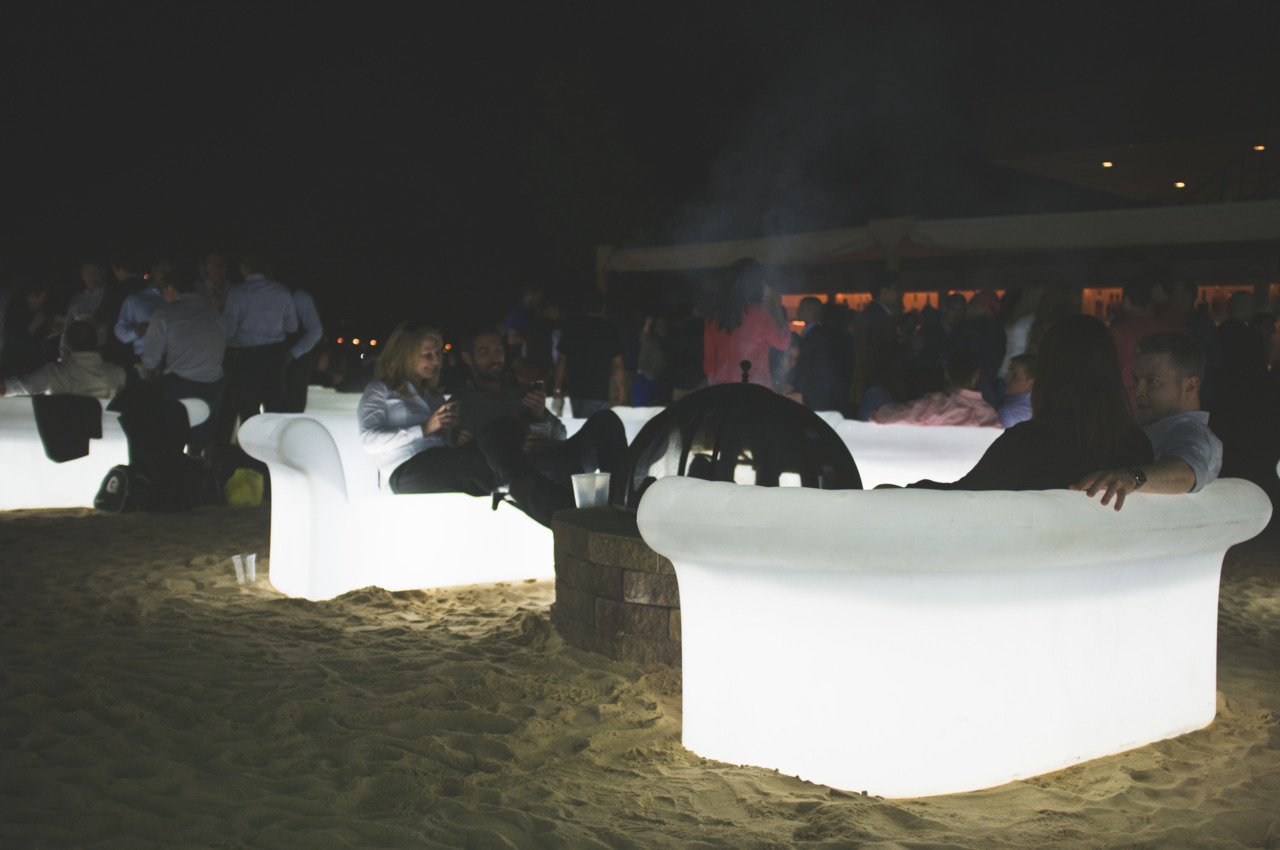 People socializing on illuminated white couches around a sand fire pit at Beekman Beer Garden in NYC.