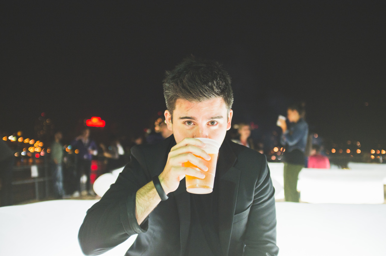 Man in a black blazer drinking while seated on an illuminated lounge bench at Beekman Beer Garden.